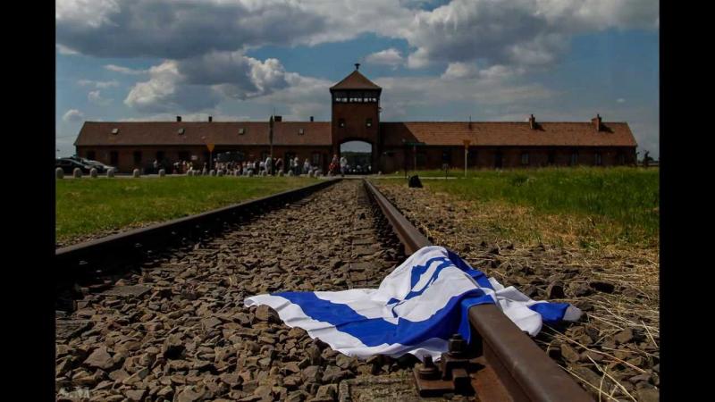 תמונה של דגל ישראל מונח על פסי הרכבת בכניסה למחנה ההשמדה אושוויץ בירקנאו בפולין